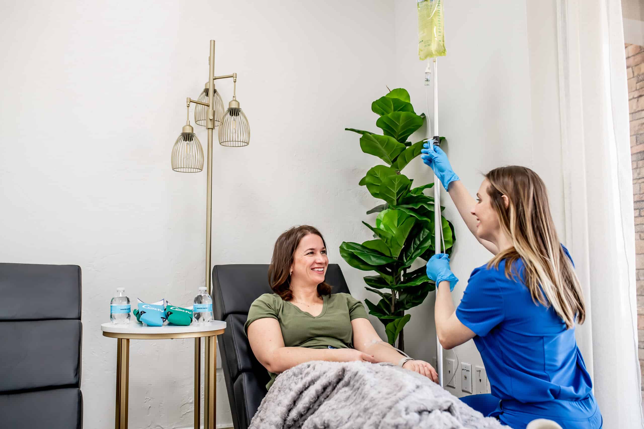 Elite Recharge IV therapy patient consultation with healthcare provider administering intravenous treatment in comfortable medical office with plants and decorative lighting